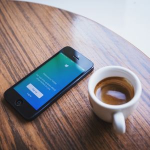 Celular com twitter aberto e café sobre a mesa