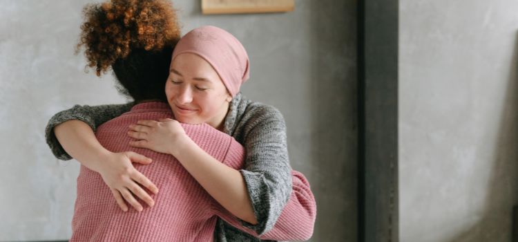 Pessoa com câncer sendo abraçada pela amiga