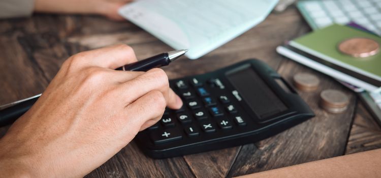 Pessoa fazendo cálculos na calculadora em cima da mesa