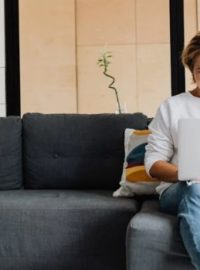Mulher sentada no sofá com notebook no colo e telefone na mão
